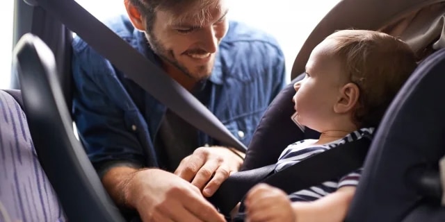man buckling baby into a car seat