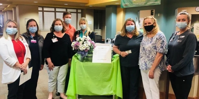 group of masked nurses stand around a table holding an award