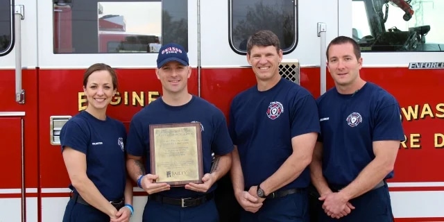 4 firefighters standing in front of their fire engine holding up an award